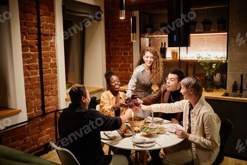 Preview: Group of young intercultural friends sitting by served table in the kitchen