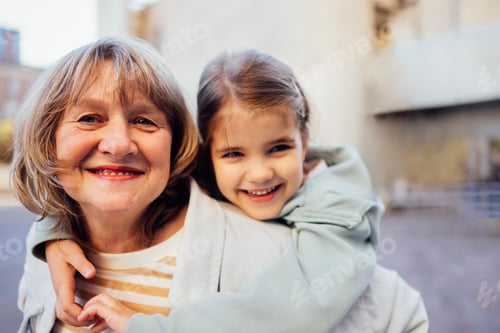 Preview: Little girl hugging smiling middle aged woman. Cute female kid and her grandmother