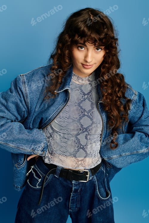 Preview: Stylish young woman showcases trendy denim in a vibrant blue backdrop