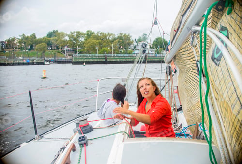 Preview: Young woman adjusting sail on sailboat, looking up