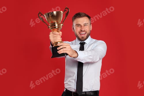 Preview: Portrait of happy young businessman with gold trophy cup on red background