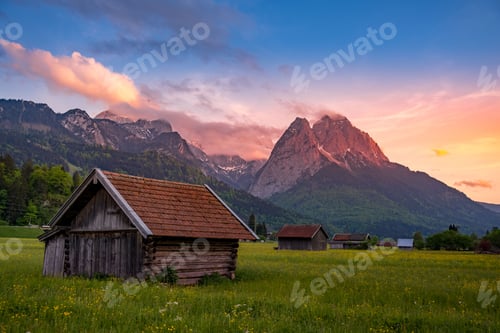 Preview: Wooden houses in the alpine ski town Garmisch-Partenkirchen captured against mountains at sunset