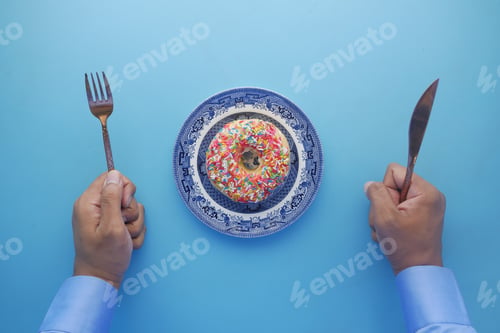 Preview: top view of man hand with knife and fork waring for eating donuts