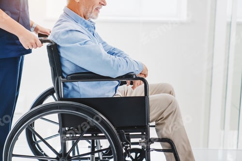 Preview: Side view cropped shot of nurse pushing injured old patient on wheelchair indoor
