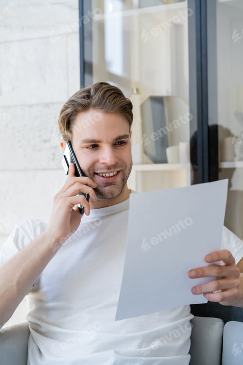 Preview: young and happy man holding white paper during conversation on smartphone