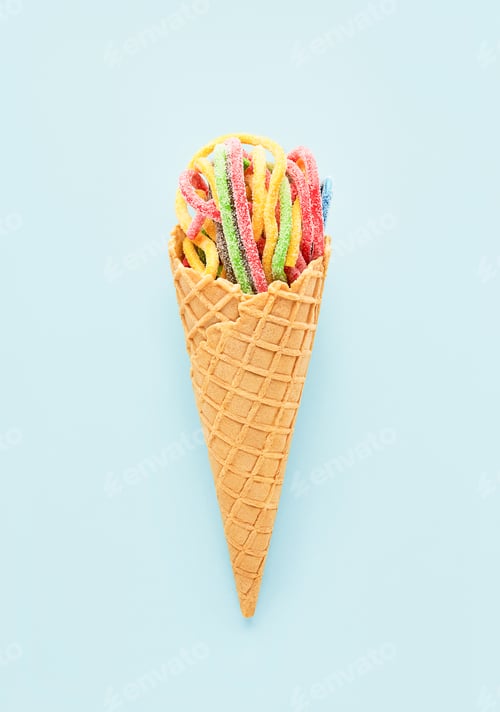 Preview: Colorful sour jelly candies in sugar sprinkles in an ice cream cone on a blue background. Vertical.