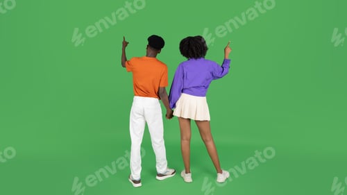Preview: Young african american man and woman in casual point fingers at empty space, enjoy date