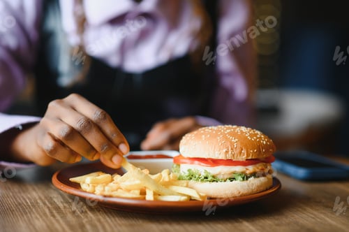 Preview: African girl eating burger and fries in cafe. Fast food concept