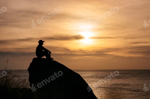 Preview: Man sitting on big rock with sightseeing of sunset in tropical sea