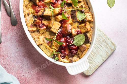 Preview: Cooling freshly baked bread pudding with raising and almond slivers in a white casserole dish.