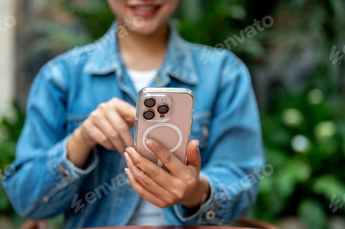 Preview: The smiling woman holding a smartphone with left hand and pointing at the screen with right hand.
