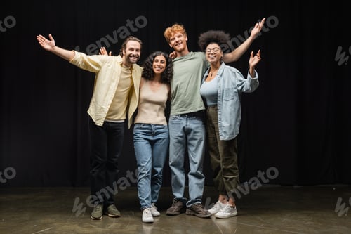 Preview: full length of cheerful interracial actors embracing while waving hands and smiling at camera in