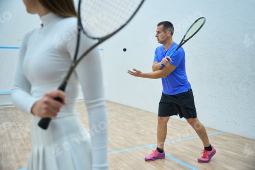 Preview: Enthusiastic man coach teaching woman accurate racket skills in squash