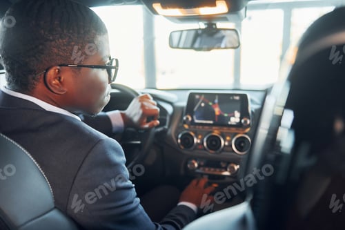 Preview: Rear view. Young african american businessman in black suit is in the automobile