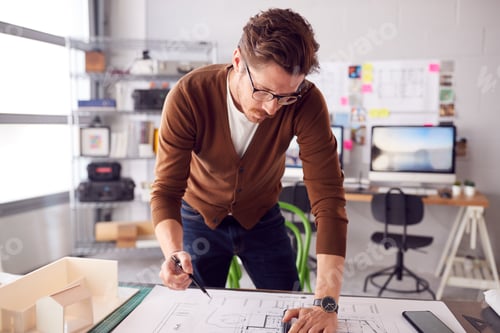 Preview: Male Architect Standing At Desk In Office Amending Building Plans