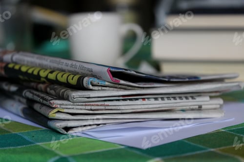 Preview: Stack of newspapers and a cup of coffee on a green tablecloth