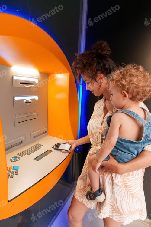 Preview: Mother withdrawing cash at ATM with her son in her arms