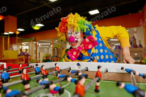 Preview: Happy excited clown with funny makeup playing table football