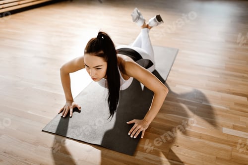 Preview: oung slim dark-haired girl dressed in white sports clothes is doing push ups in the gym