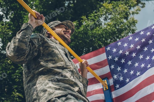Preview: low angle view of soldier pulling himself up on crossbar with american flag on backdrop