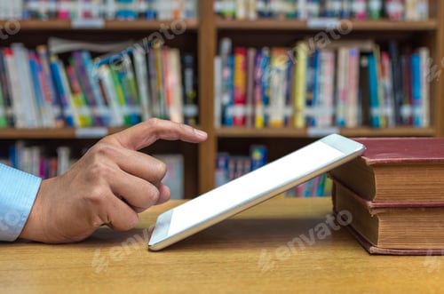 Preview: Finger pointing on the screen of tablet computer over the wood table in library