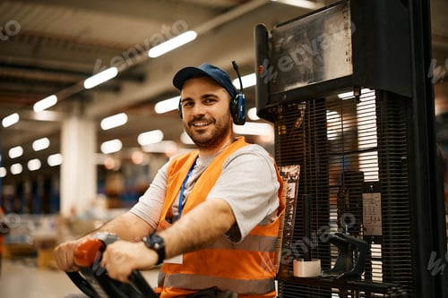 Preview: Happy warehouse worker driving pallet jack and looking at camera.