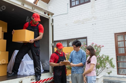 Preview: Young couple checks with two movers unloading boxes and furniture from a pickup truck