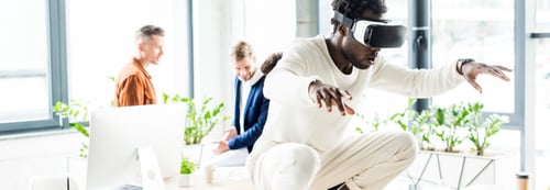 Preview: panoramic shot of african american businessman using vr headset and squatting on desk while