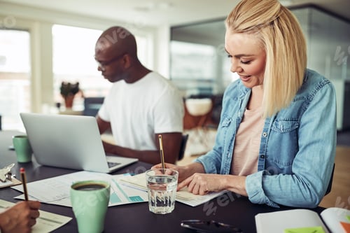 Preview: Smiling young businesswoman working at an office table with colleagues
