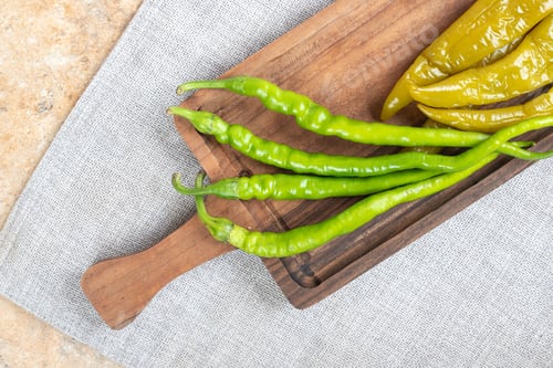 Preview: Pickled and fresh green peppers on wooden board