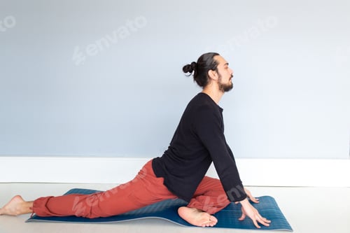 Preview: Young Caucasian long haired white man is performing yoga in a studio or house.