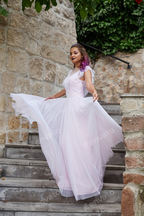 Preview: Beautiful woman with purple hair in a white wedding dress walks in the garden. Natural makeup