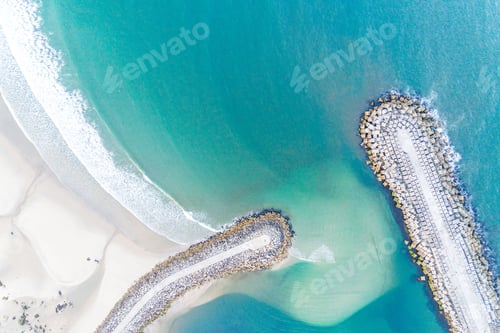 Preview: Aerial view of a beach with turquoise waters and two rock jetties extending into the ocean.