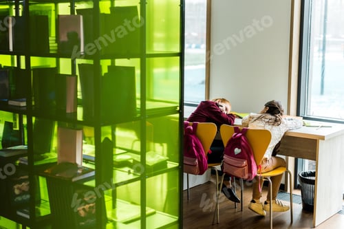 Preview: back view of bored schoolgirls lying on table in library