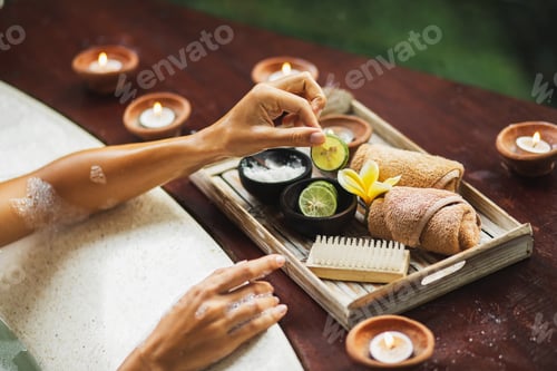 Preview: Beauty spa treatment concept. Woman hands hold lime from natural cosmetics set on wooden tray
