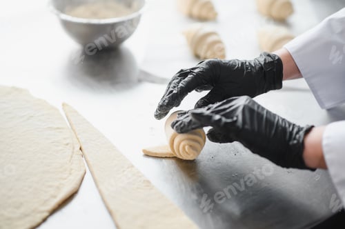 Preview: Baker rolling dough for croissant in bakery kitchen