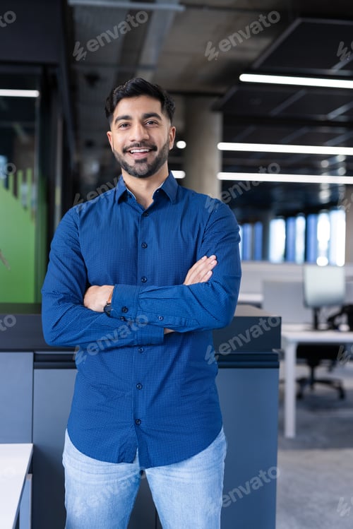 Preview: Smiling businessman in modern office, standing with arms crossed, wearing blue shirt