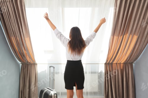 Preview: Woman enjoying morning light in hotel room near a window with open curtains