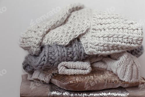 Preview: Close up of neatly folded knitted items of pastel color on a light background.