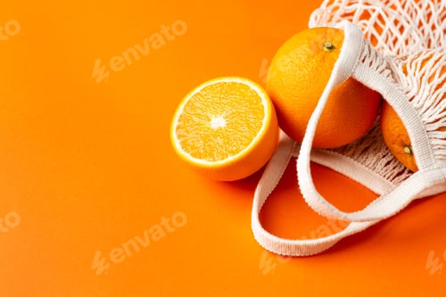 Preview: Cutting orange in cotton shopping eco friendly bag on orange background.