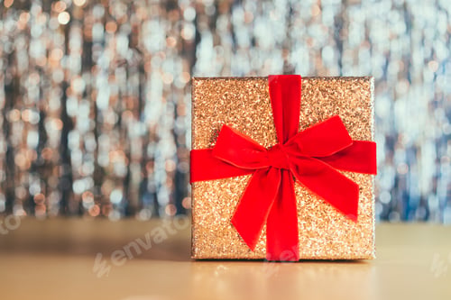 Preview: Glittering golden gift box with velvet red ribbon on sparling shining background. Festive concept