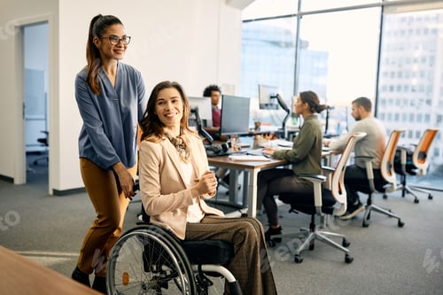 Preview: Happy businesswoman assisting her colleague in wheelchair through the office.
