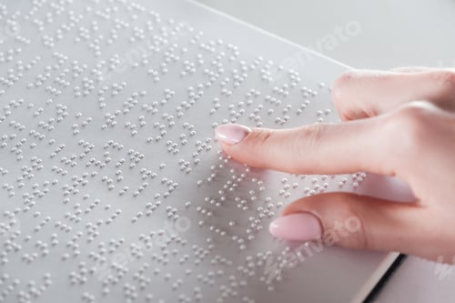 Preview: partial view of young woman reading braille text on white paper