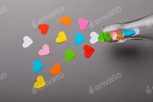 Preview: Glass bottle pouring colorful heart shaped papers on gray background with copy space