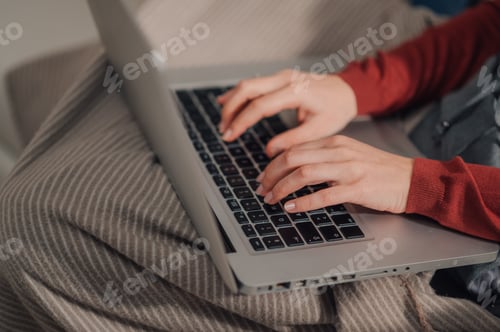 Preview: Woman working remotely from home typing on laptop keyboard on cozy blanket