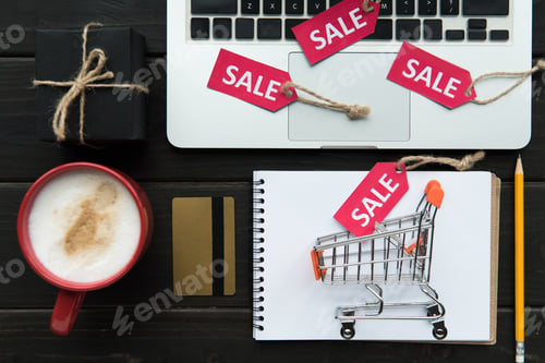 Preview: top view of laptop on table with coffee, credit card, little shopping cart and sale tags