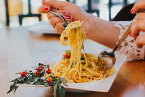 Preview: High angle shot of female hands with fork and spoon taking spaghetti carbonara from white plate