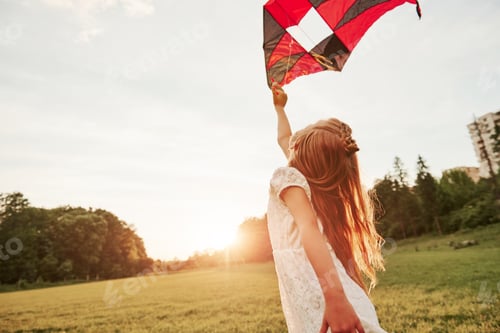 Preview: City is nearby. Happy girl in white clothes have fun with kite in the field. Beautiful nature