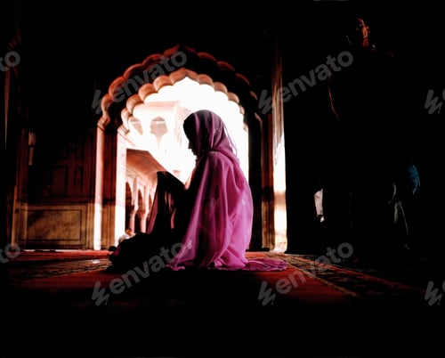 Preview: Woman wearing a pink veil and sari sitting on the floor covered with carpet. Scalloped archway. Deep