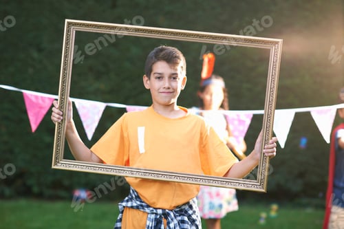 Preview: Portrait of boy looking through picture frame, looking at camera
